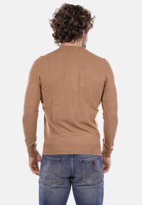 Maglione lavorato a maglia color beige con un design aderente e polsini a costine, mostrato da dietro. Abbinato a jeans in denim blu, che mostrano semplici dettagli di cucitura.