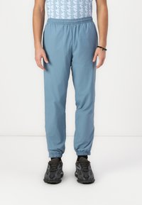 Lichtblauwe joggers met elastische tailleband en taps toelopende boorden, gemaakt van ademende stof. Draag ze met zwarte sportschoenen met een gestructureerd patroon.