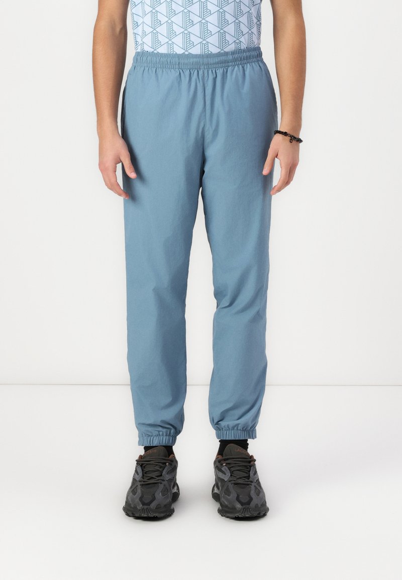 Lichtblauwe joggers met elastische tailleband en taps toelopende boorden, gemaakt van ademende stof. Draag ze met zwarte sportschoenen met een gestructureerd patroon.