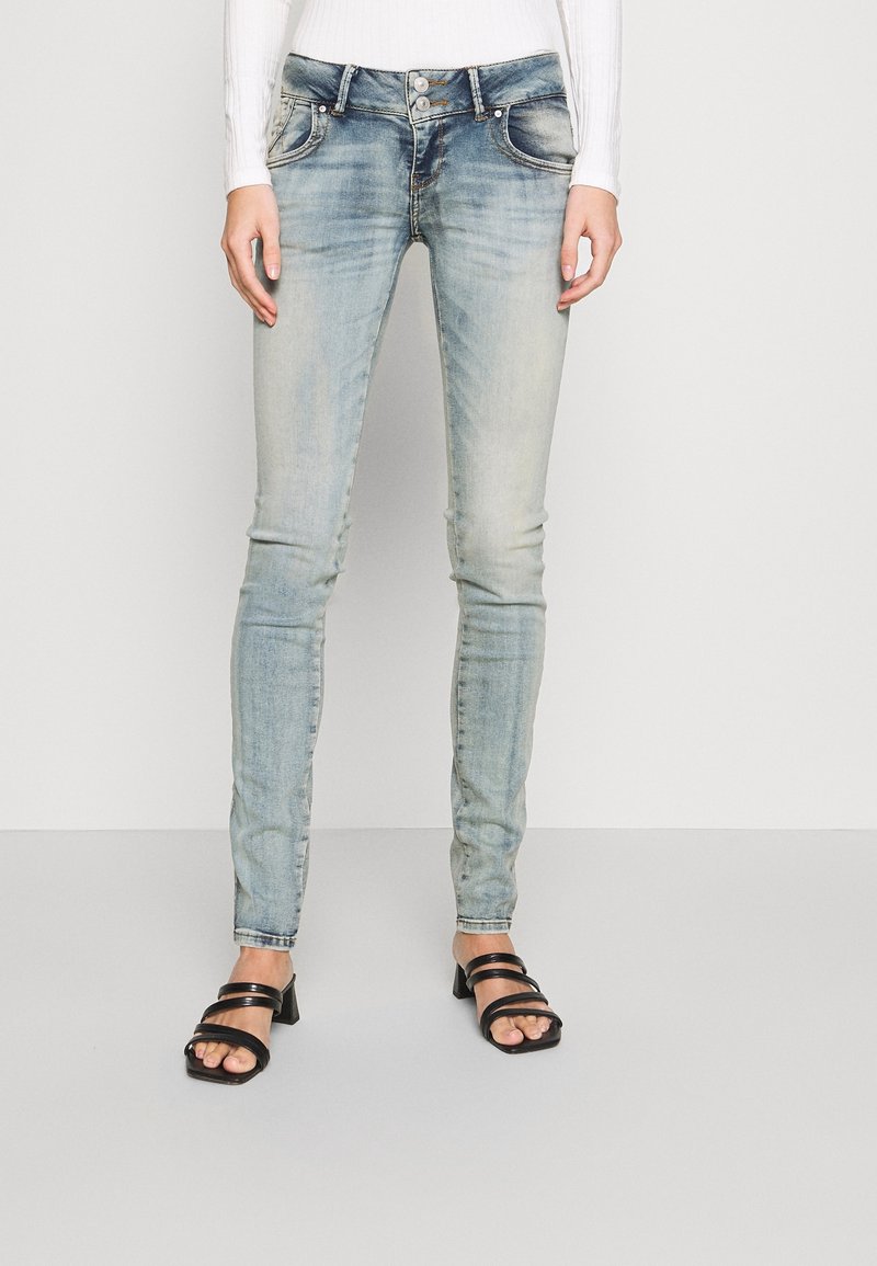 Jean bleu clair, coupe ajustée, texture délavée, deux poches avant et fermeture à bouton. Associé à des sandales à talons noires à lanières.