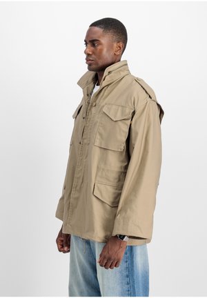 Beige utility jacket featuring a high collar, multiple flap pockets, and relaxed fit. Made from lightweight fabric with a smooth texture.