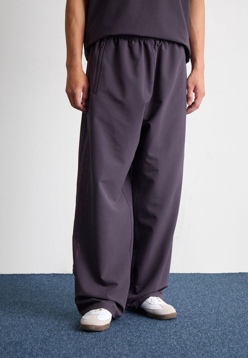 Tmavě šedé, volné tepláky s elastickým pasem a bočními kapsami, které mají jemný perforovaný design podél vnějších švů.