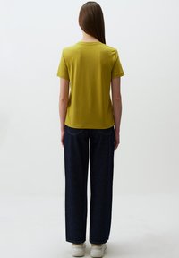 Oliwkowy t-shirt z krótkim rękawem wykonany z miękkiej tkaniny; zestawiony z wysokim stanem ciemnoniebieskich szerokich spodni dżinsowych i białymi sneakersami.