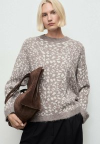 Pull gris clair avec des motifs abstraits blancs, col rond et coupe loose. Sac en suède marron de forme courbée avec des poignées courtes.
