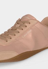 Gros plan d'une sneaker rose blush Calvin Klein avec des lacets assortis et une semelle en caoutchouc texturée marron clair.
