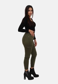 Oliwkowe spodnie typu cargo z zamkami w kieszeniach i ściągaczami u dołu, zestawione z czarnymi botkami na obcasie, zdobionymi kryształkami i gładkim wykończeniem.