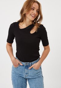 T-shirt nera a coste con maniche corte e un'apertura circolare sulla spalla. Abbinata a jeans in denim azzurro chiaro a vita alta.