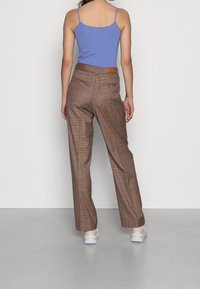 Bruna rutig byxa med avslappnad passform, som har en hög midja med en brun läderpatch, åtföljd av en ljusblå linne.