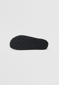 Semelle de chaussure en caoutchouc noir présentant un motif ondulé, épousant les contours sur les bords, avec une surface texturée pour une meilleure adhérence.