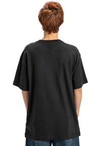 Čierne bavlnené tričko s krátkym rukávom, voľný strih a okrúhly výstrih. Má hladký povrch a jednoduchý dizajn, zobrazené zozadu.