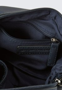 Interno di una borsa navy con una fodera in tessuto liscio, tasca con zip e un'etichetta in pelle con testo impresso. Materiale esterno texturizzato visibile.