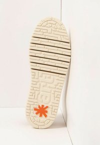 Semelle extérieure de baskets blanches avec des rainures texturées et un logo "abc" en relief. Présente un accent d'astérisque orange près du talon.