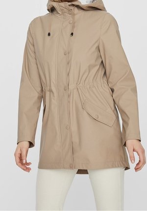 Beige hooded raincoat with front snap buttons, adjustable waist, flap pocket, and long sleeves worn over white pants.
