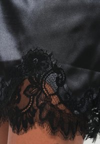 Fekete szatén szövet virágos csipkés szegéllyel az alján, bonyolult mintákkal és puha tapintással.