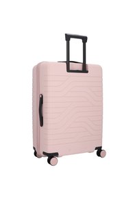 Valigia rigida di un delicato rosa pallido, caratterizzata da linee ondulate texturizzate, manico retrattile nero e quattro ruote con accenti rosa per facilitare la mobilità.
