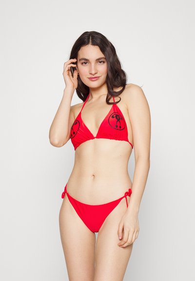 Biquíni vermelho com um topo triangular, apresentando padrões circulares pretos. A parte de baixo tem laterais ajustáveis com cordão e uma textura suave.