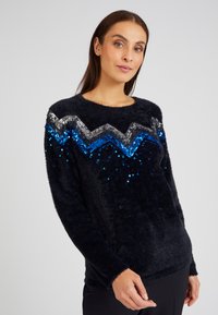 Flauschiger schwarzer Pullover mit einem Pailletten-Zickzack-Muster in Silber und Blau über der Brust, langen Ärmeln und rundem Ausschnitt.
