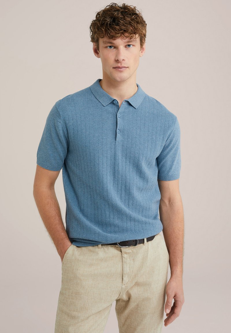 Polo de manga corta en azul claro con un patrón diagonal texturizado, que presenta un cuello con solapa y una tapeta de tres botones, combinado con pantalones beige.