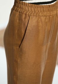 Lichte, bruine broek met een elastische tailleband, voorzien van zijzakken en een gladde, licht gestructureerde stof.