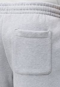 Pantalon de survêtement gris clair avec une taille élastique et une poche arrière rectangulaire cousue sur le côté droit.