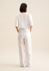 Witlinnen top met een keyhole detail aan de achterkant, gecombineerd met hoge witte linnen broek met twee achterzakken en knoopaccenten.