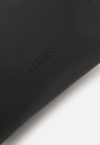 Black waterproof bag made of matte rubberized material, featuring embossed "RAINS" logo, smooth texture, and a minimalist design.
