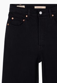 Zwarte denim jeans hebben een rechte snit, vijf zakken en koperen hardware. De stof heeft een gladde textuur met subtiele stiksel details.