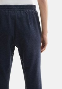 Pantalons de jogging bleu marine en tissu texturé, dotés d'une taille élastique avec coutures horizontales et d'une coupe ample. Zone de poche visible à l'arrière.