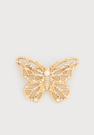Spilla a forma di farfalla in oro con ali traforate aperte, adornata con piccole perle e strass trasparenti su sfondo bianco.