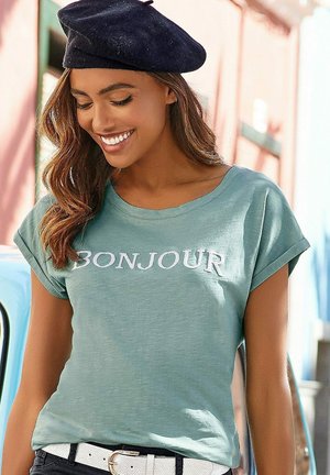 T-Shirt in Mintgrün mit der Aufschrift "BONJOUR" in weißer Schrift. Kurze Ärmel, lockere Passform, kombiniert mit einem schwarzen Baskenmütze und einem weißen Gürtel.