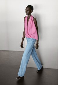 Roze mouwloze top, losse fit, met een diepe V-hals; gecombineerd met lichtblauwe wijde jeans en zwarte sandalen met decoratieve accenten.