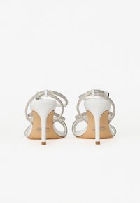 White high-heeled sandals with silver strappy detailing. Features a smooth leather finish and slender stiletto heels.