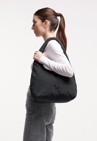 Borsa a spalla nera oversize con una texture liscia e morbida, caratterizzata da un logo discreto e da una tracolla larga per un facile trasporto.