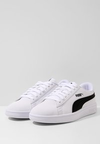 Vita sneakers med en slät syntetisk ovandel, svarta sidodetaljer och en logotyp. Utrustade med snörning och en vadderad sula.