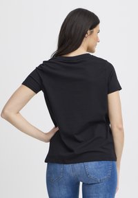 Fekete rövid ujjú póló kerek nyakkivágással, pamut anyagból. Laza fazonú és sima textúrájú, farmernadrággal párosítva.