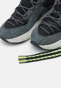 Grå och svarta sneakers med en texturerad överdel i mocka och mesh, med en vitprickig sula. Inkluderar snören i neongrön och svarta ränder.