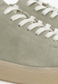 Jasnozielone zamszowe sneakersy z białymi sznurówkami, o zaokrąglonym kształcie, minimalnym przeszyciu i teksturowanej gumowej podeszwie. Widok z góry pokazuje detale cholewki.