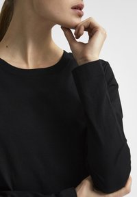 Maglietta nera a maniche lunghe con scollo arrotondato, realizzata in morbido cotone liscio e con cuciture visibili sulle maniche.