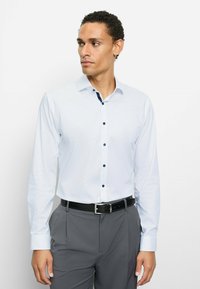 Langärmliges weißes Hemd mit marineblauen Knöpfen und Kragenakzenten, kombiniert mit grauer Hose und schwarzem Gürtel. Glatter Stoff und maßgeschneiderte Passform.