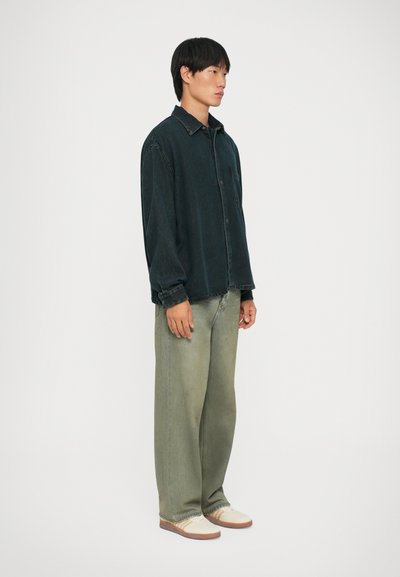 Mørkegrønn denimskjorte, litt oversized med knapper foran og krage. Brukt med olivengrønne vide bukser og kremfargede sko.