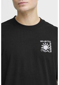 Sort bomulds t-shirt med et hvidt sol- og bølgedesign samt teksten "UNLIMITED SUMMER" på venstre brystområde. Klassisk crew neck design.