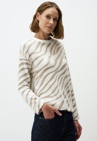 Witte trui met een zachte, fuzzy textuur en een beige gestreept zebrapatroon. Lange mouwen en een ronde halslijn, gedragen over donkere spijkerbroeken.