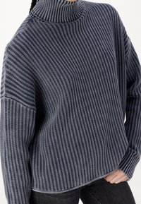 Pull à col roulé épais bleu marine avec une texture côtelée, des coutures latérales marquées et des épaules tombantes. Coupe décontractée, idéale pour le superposition.