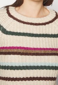 Stickad tröja med krämfärgad bas och horisontella ränder i mörkgrön, brun, ljusblå och rosa. Ribbade ärmslut med texturdetalj.