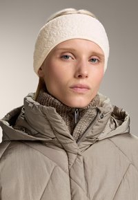 Beige vadderad jacka med hög krage och huva, ihop med ett texturerat cremefärgat fleece-pannband med släta kanter och en åtsittande passform.