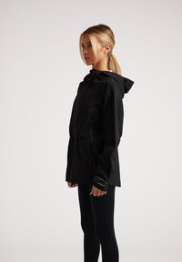 Svart vattentålig jacka med huva, dragkedja fram och justerbara ärmar. Designen är elegant med en minimalistisk estetik.