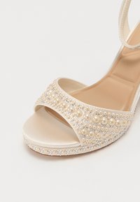 Sandale à talon haut beige à bout ouvert, décorée de perles et de strass sur la bride et la plateforme.