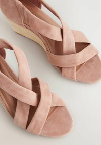Sandali con zeppa in suede rosa, con design a tracolla incrociata, tessuto testurizzato e suola imbottita; presenta una base naturale simile alla paglia intrecciata.