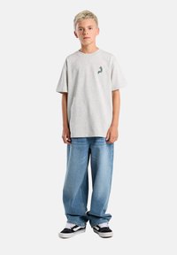 Gray cotton t-shirt with a small blue and orange design on the chest, paired with loose blue denim jeans and black and white sneakers.