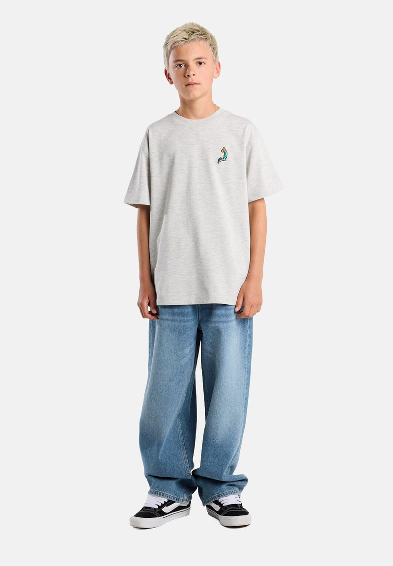 Gray cotton t-shirt with a small blue and orange design on the chest, paired with loose blue denim jeans and black and white sneakers.